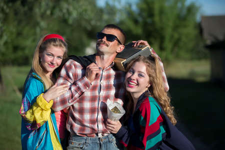 Funny man with cassette recorder hugs girls. People in the style of the nineties.の写真素材