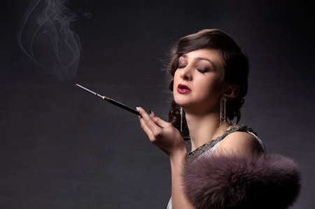 Retro woman portrait. A beautiful woman in the style of the 20s and 30s with a cigarette holder smokes.の写真素材