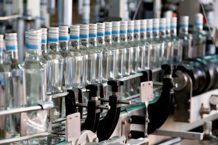 A long row of glass bottles on a conveyor belt. Production of alcoholic beverages.