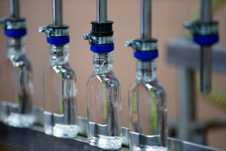 A row of glass bottles on a conveyor belt for the production of alcoholic beverages.