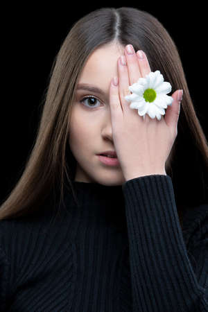 A beautiful girl with natural beauty holds a white flower near her eye. Young girl with a white...
