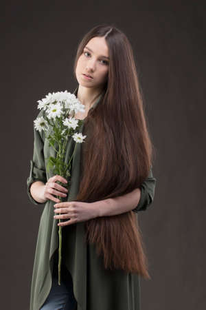 A beautiful young girl with natural beauty with long smooth hair holds a bouquet of white chrysanthemums.の写真素材