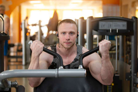 A handsome young strong man of an athletic physique is engaged on a sports simulator.