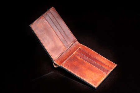 Open leather brown purse with pockets on a dark background.