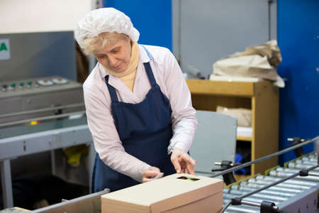 March 19, 2021 Belarus, Gomil. Plant for the production of alcoholic beverages. Packaging conveyor. A woman packer is packing goods in a box.のeditorial素材