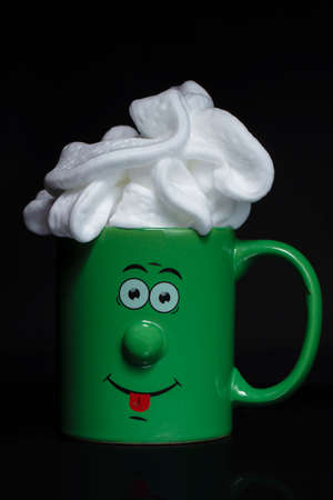 Funny green cup with a cheerful face with whipped cream. An invigorating drink in the morning.の写真素材