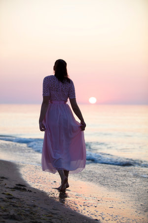 Silhouette of a woman in a pink dress at sunset on the sea.の写真素材