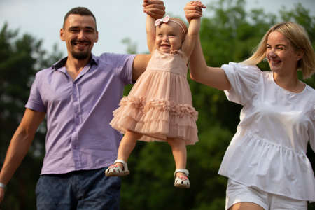 Husband, wife and their little daughter for a walk in the park. Happy dad and mom throws up their little laughing one-year-old daughter.の写真素材