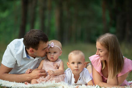 Husband and wife and their little children. Family portrait in nature. Mom and Dad with their brother and sister are lying on the grass. Young family with children for a walk.の写真素材