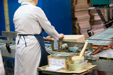 March 19, 2021 Belarus, Gomil. Plant for the production of alcoholic beverages. Packaging conveyor. A woman packer is packing goods in a box.のeditorial素材
