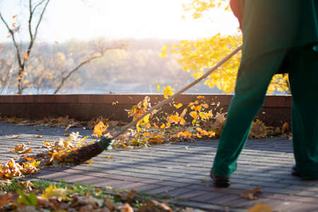 A worker cleans the street with a broom. A janitor cleans the road of fallen leaves in the fall. Utility worker with broom cleaningの写真素材