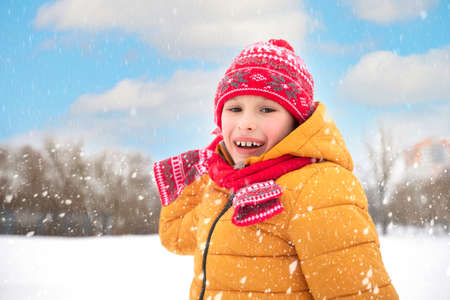 Funny little boy in colorful clothes playing outdoors during a snowfall. Active holidays with...