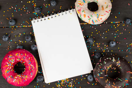 On a wooden background, blank notepad, colorful donuts and blueberries. Creative cuisine.