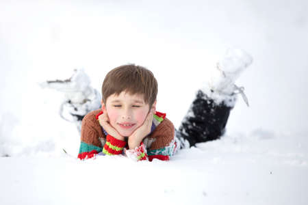 A funny little boy in colorful clothes lies in the snow. A hardened child in winter.の写真素材