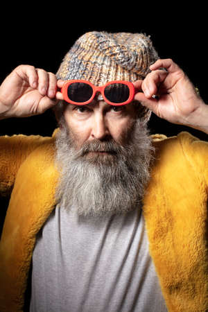 Vertical portrait of an elderly man wearing fashionable clothes and red glasses.