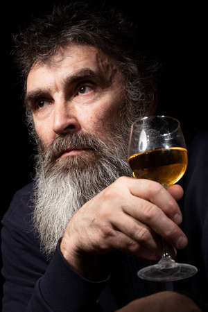 Portrait of a sad elderly man with a gray beard with a glass of cognac.