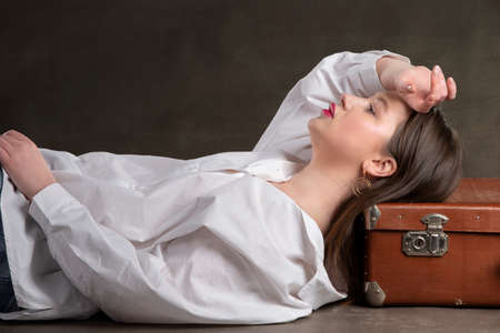 A beautiful girl lies on an old suitcase on a gray background.の写真素材