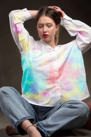 A beautiful girl in a multi-colored shirt and jeans on a gray background.の写真素材