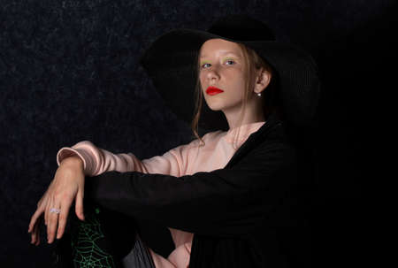 A teenage girl in a black hat dressed up for the holiday of halloween.