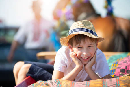 A funny little boy in a straw hat lies on a cart looking at the camera and smiles.