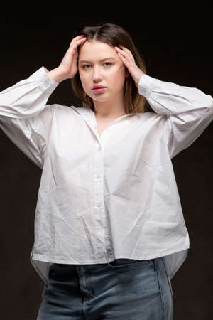 Beautiful girl in a white shirt and jeans on a dark background posing at the camera.の写真素材