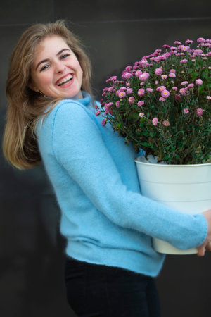 A beautiful girl is holding a large bouquet of flowers and smiling. Happy young woman in the city.の写真素材