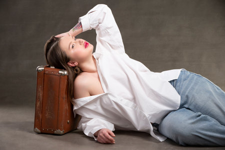 Beautiful girl with an old suitcase on a gray background.の写真素材