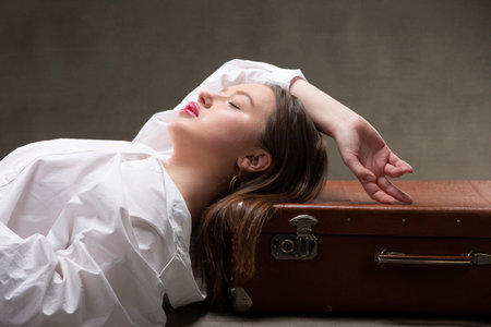 A beautiful girl lies on an old suitcase on a gray background.の写真素材
