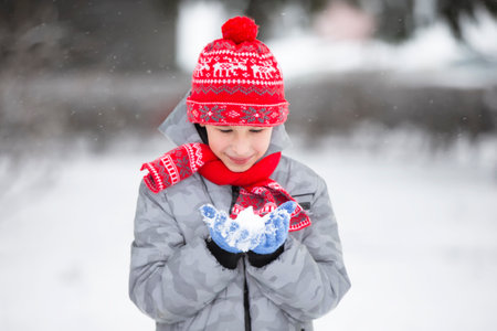 Happy boy holding snow in his hand. The child rejoices in winter and the first snow.の写真素材