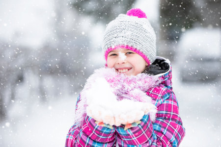 Happy girl holding snow in her hand. The child rejoices in winter and the first snow.の写真素材