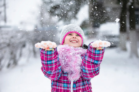 Happy girl throw snow. The child rejoices in winter and the first snow.の写真素材