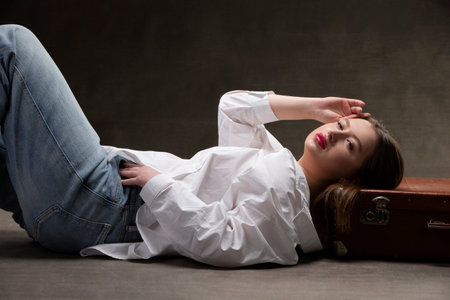 A beautiful girl lies on an old suitcase on a gray background.の写真素材