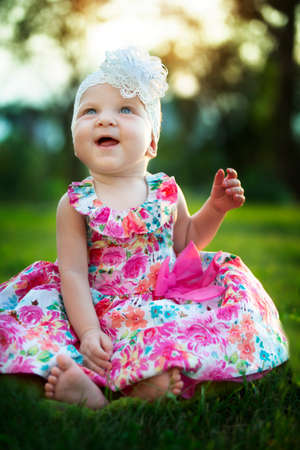 Happy little girl sits on the grass and laughs. beautiful child. Little baby up to a year old on a summer meadow.の写真素材