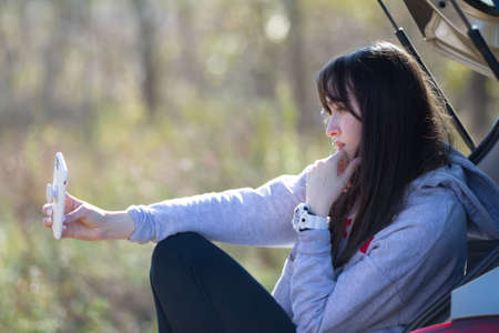 Portrait of a beautiful girl outdoors who uses a smartphone, shares digital content with each other...
