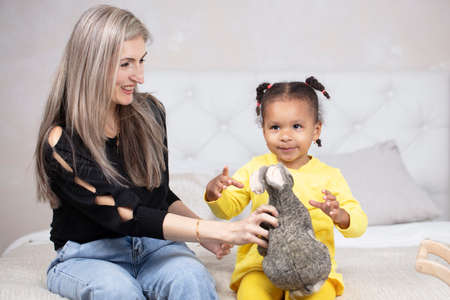 Multiethnic mom and daughter play at home. Cheerful mother with little daughter of African...
