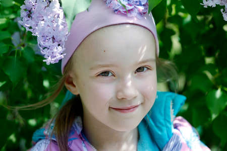 Belarus, Gomil city, May 16, 2016. City street. A beautiful little girl stands by a lilac bush and smiles.のeditorial素材