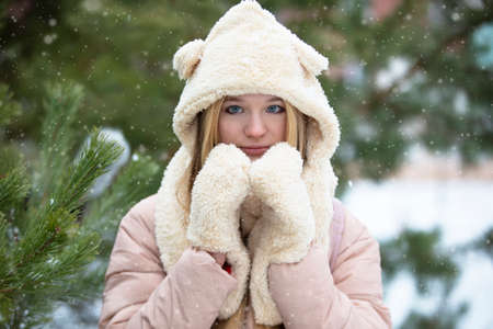 Beautiful girl in a fur hat and mittens on a winter background.