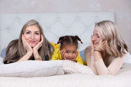 Family from different races. Mom grandmother light-skinned and a little African American girl lie on the sofa.の写真素材