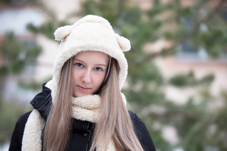 Portrait of a fair-haired teenage girl in a fur hat on a winter day.