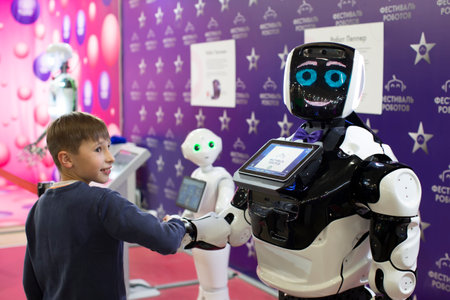 The boy is talking, playing with an android robot at the exhibition. The child greets the robot.