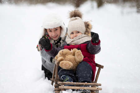 Children ride on a vintage wooden sled against the backdrop of a winter forest. Child on a winter...