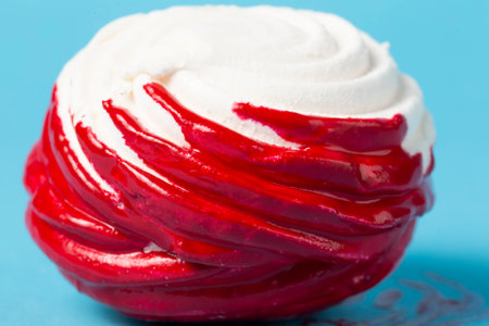 White marshmallow covered with red icing on a blue background close-up.の写真素材