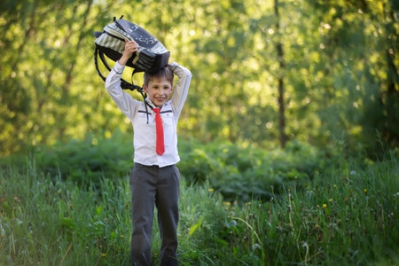 A happy schoolboy with a briefcase walks from school through a green park.の写真素材
