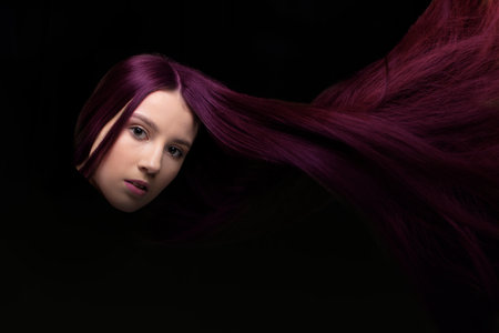 Loose flying hair. A woman with magenta hair looks at the camera on a dark background.の写真素材