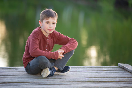 A handsome happy boy is sitting on a wooden bridge.の写真素材