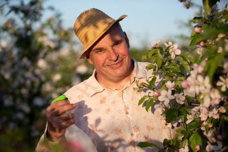 An elderly man in a straw hat in a flowering garden with a sprayer.の写真素材