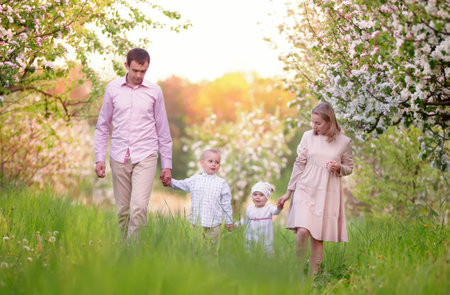 Happy parents mom and dad, daughter and son, young family outdoors in spring against the backdrop of blooming apple and cherry treesの写真素材