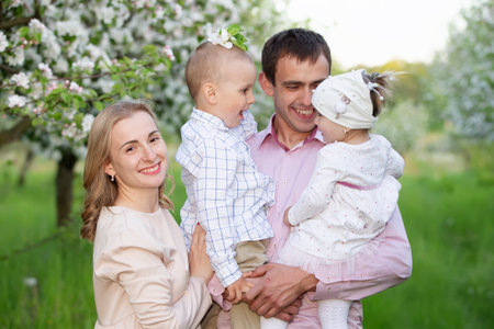 Happy parents mom and dad, daughter and son, young family outdoors in spring against the backdrop of blooming apple and cherry treesの写真素材