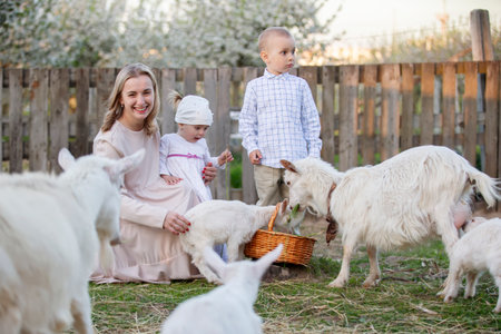 Mom with a little daughter feeds a goat. Woman with children on the farm. Family with goats. Village life.の写真素材