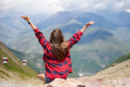 Happy woman tourist on the top of the mountain raised her hands up, enjoys the beautiful views of the mountains.の写真素材